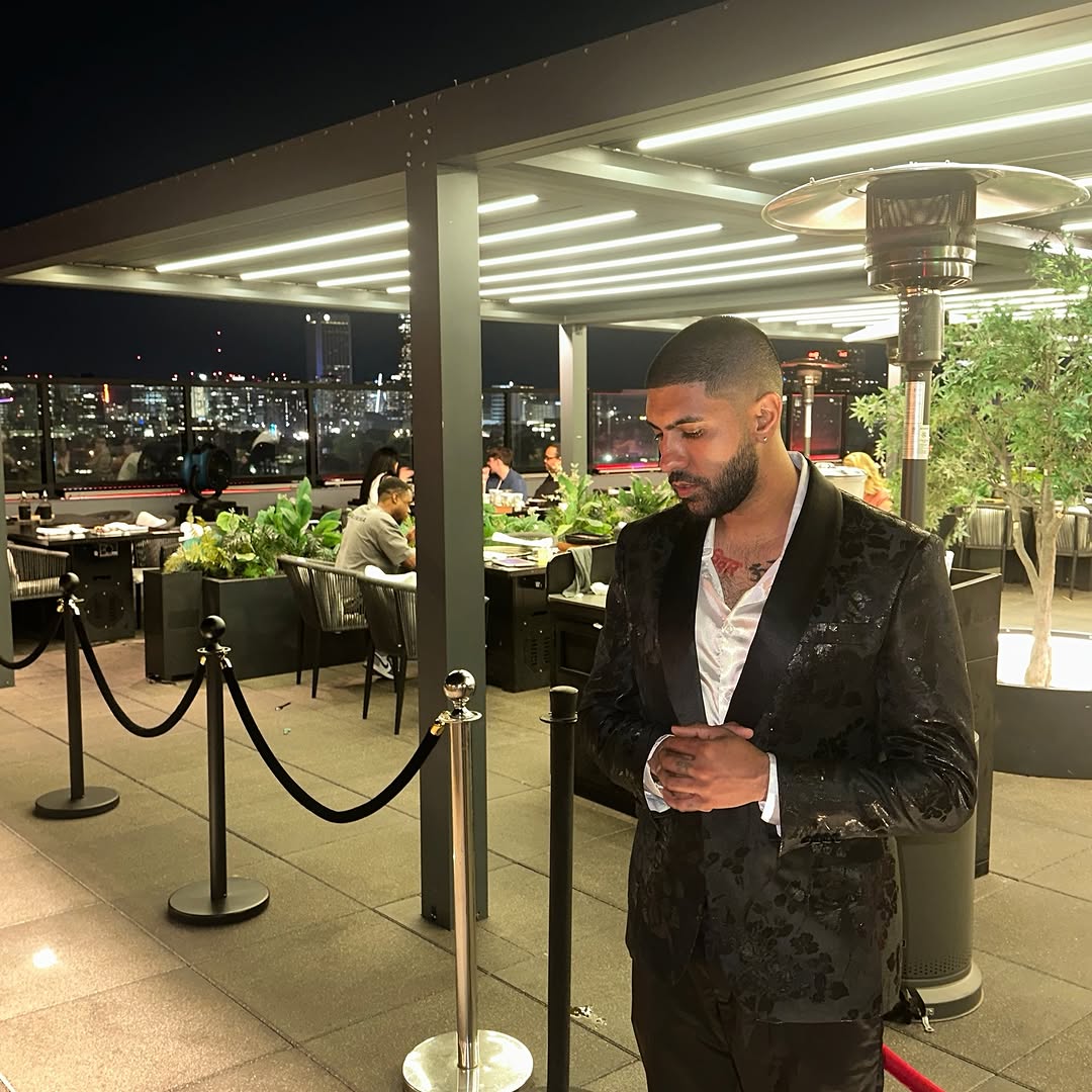 DJ Aladdinn in a black floral suit on a rooftop overlooking the Atlanta skyline