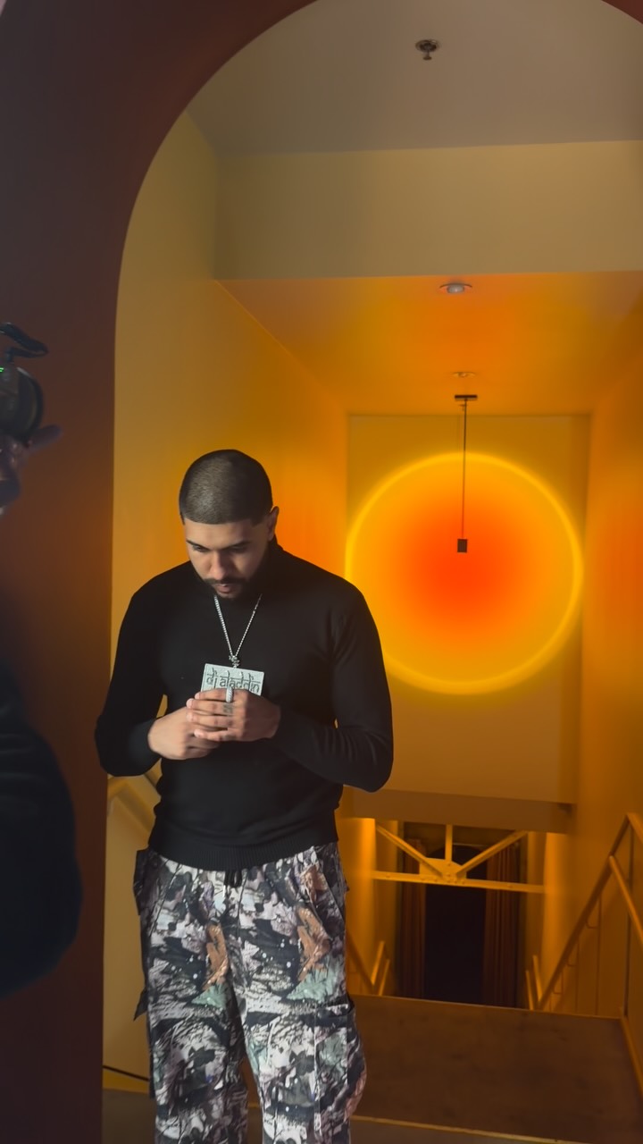 DJ Aladdinn posing for a content shoot with a glowing sunset-lamp backdrop